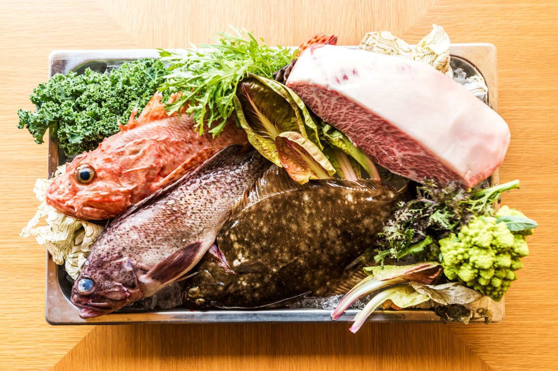 Fresh fish and seafood with vegetables arranged on a wooden board at Lull restaurant.