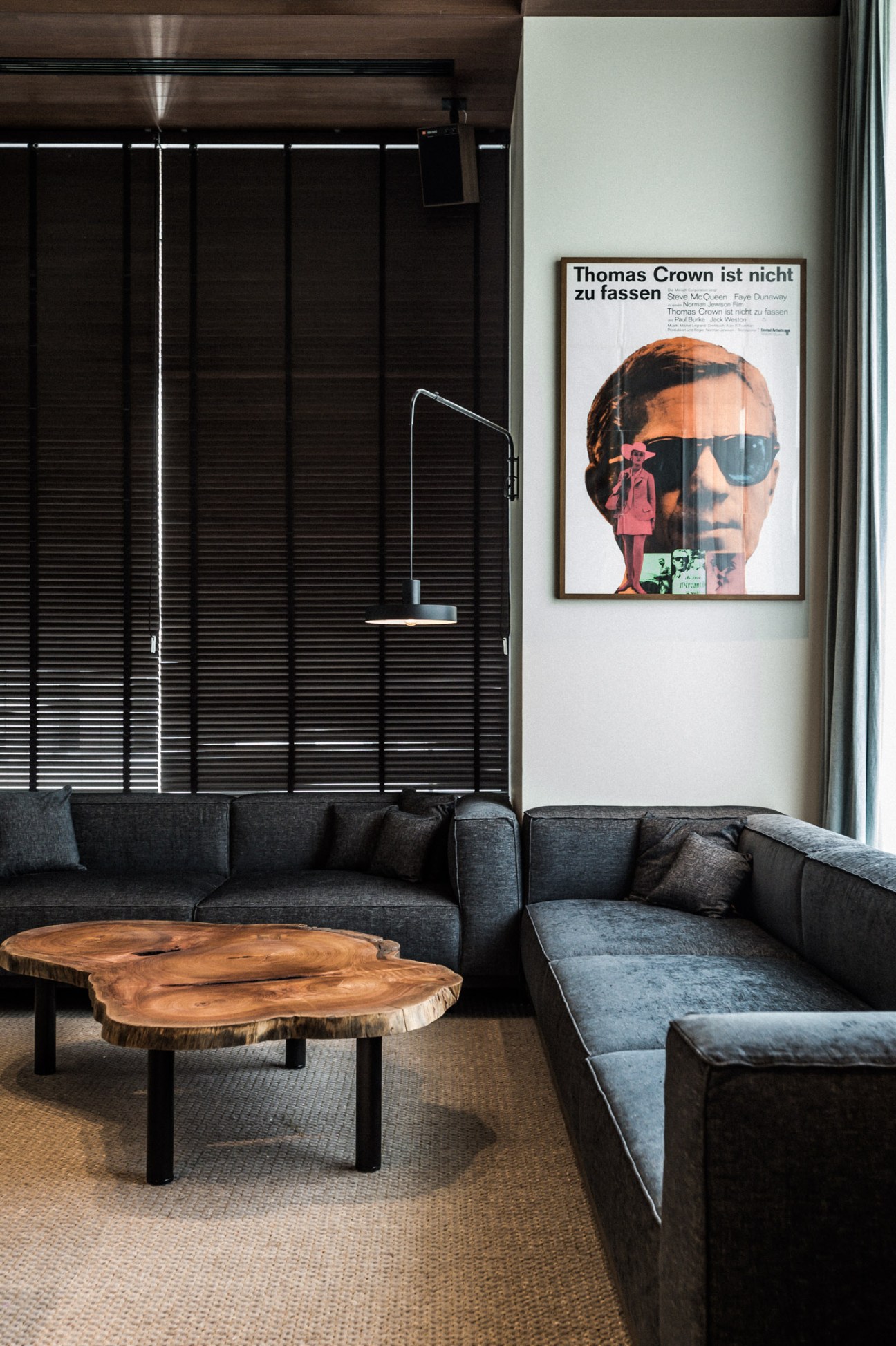 Modern hotel lounge with dark sofa, wooden coffee table, and vintage movie poster on white wall.