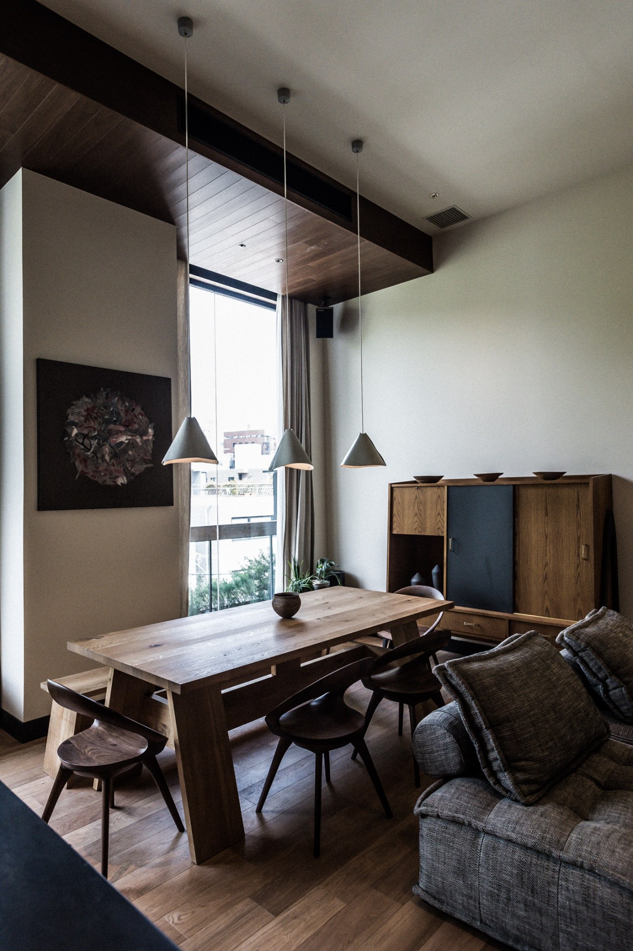 Kitchen Suite dining area with wooden table, black chairs, pendant lights from New Light Pottery, and city views.
