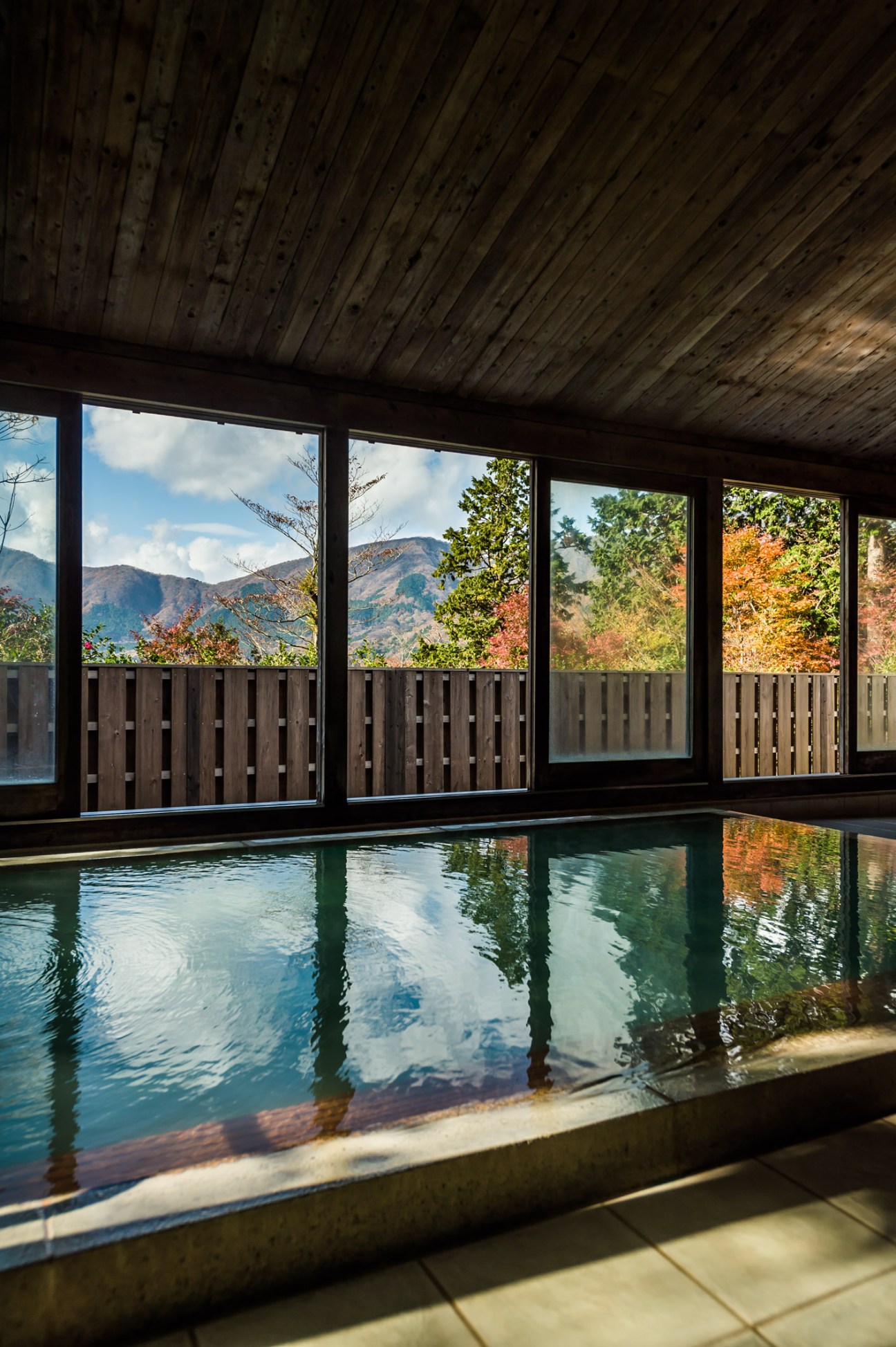 Indoor onsen bath with mountain views through large windows and wooden architectural elements