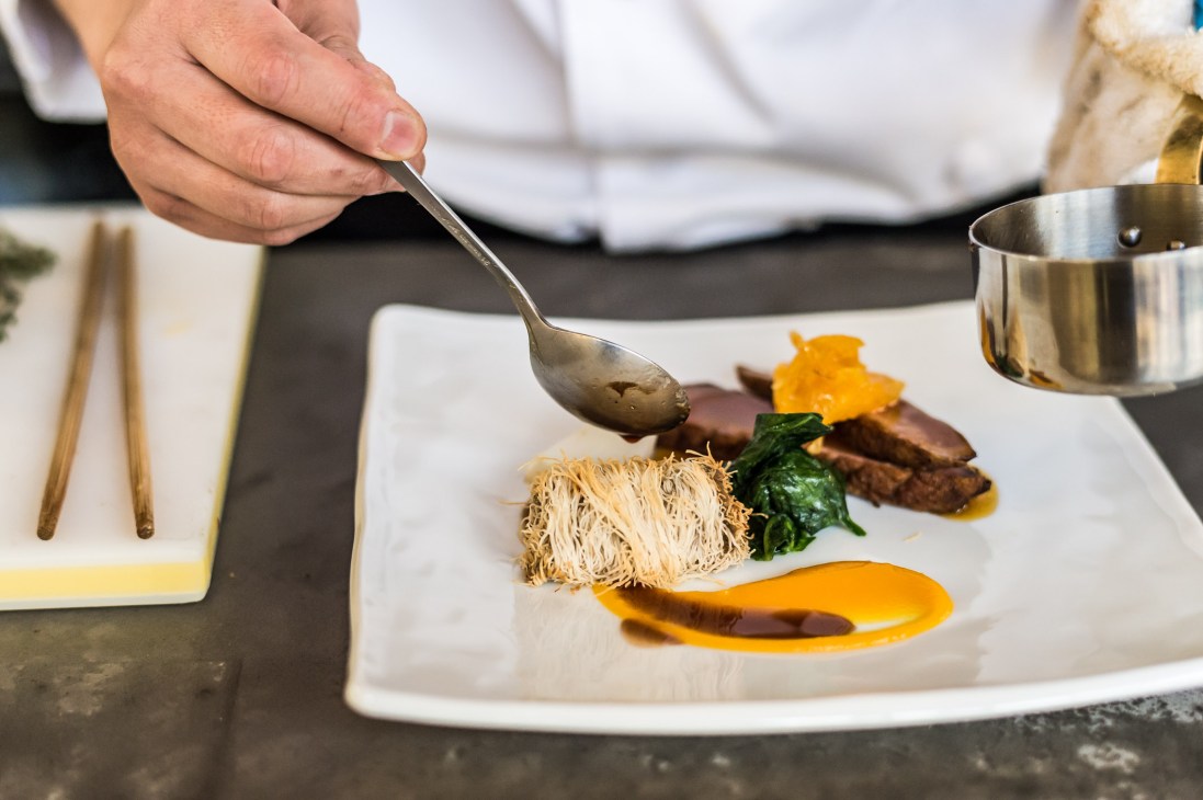 Chef plating a fine dining dish with noodles, meat, and yellow garnish at Woodside Restaurant.