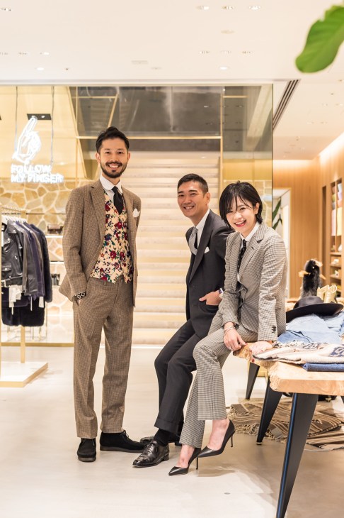 Three smiling people in business attire pose in a modern retail clothing store.