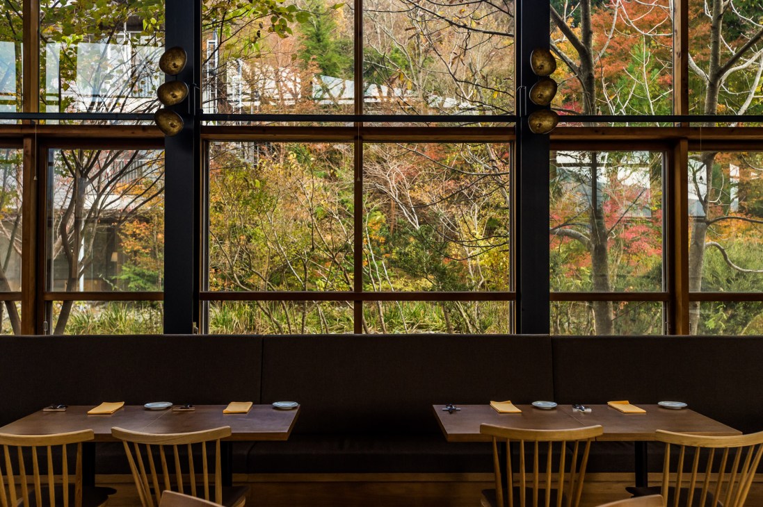 Woodside Restaurant dining room with wooden tables, chairs, and large windows overlooking autumn forest.