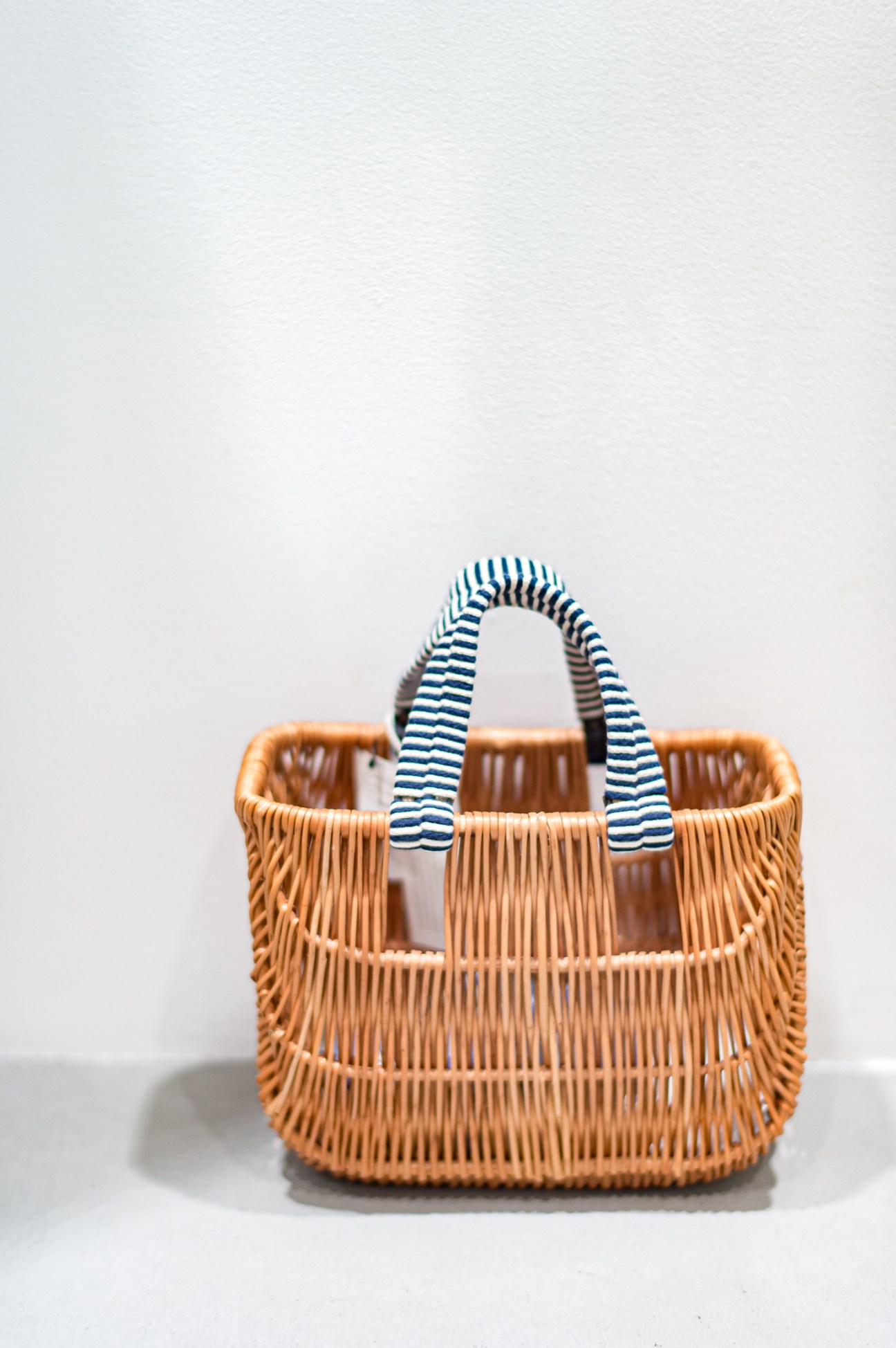 Woven wicker basket with blue and white striped fabric handles against white background