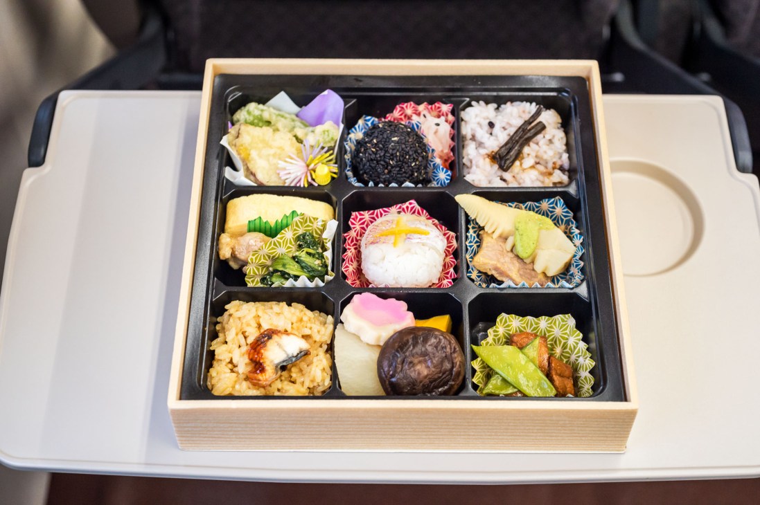 A multi-compartment bento box with nine sections containing various Japanese dishes served on a Shinkansen train.