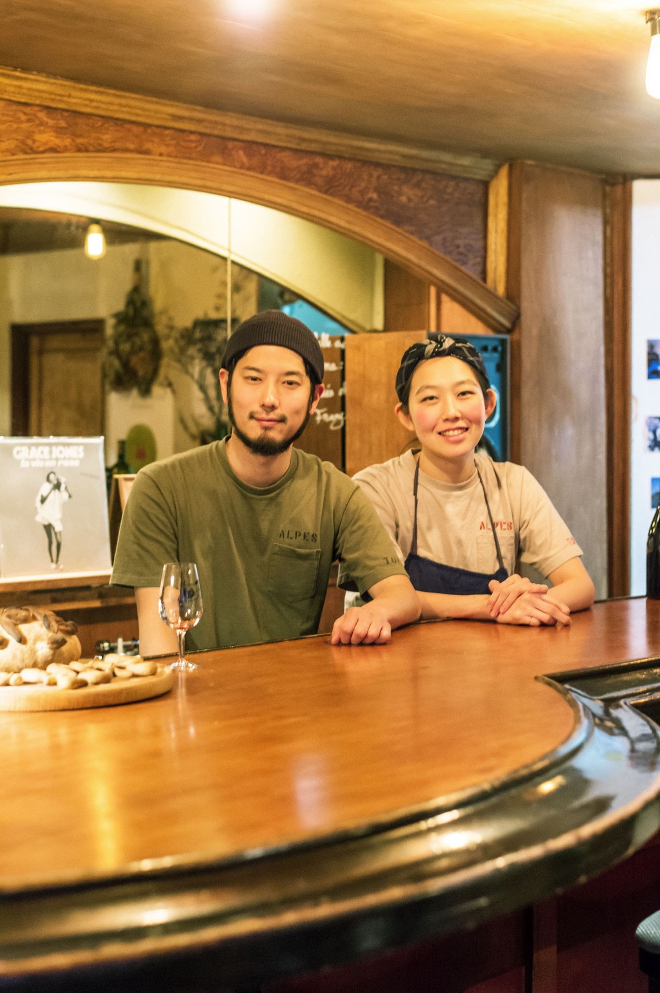 Shigeki and Haruka Ikezaki stand behind a wooden bar counter at Wine Bar Alpes in Toyama.