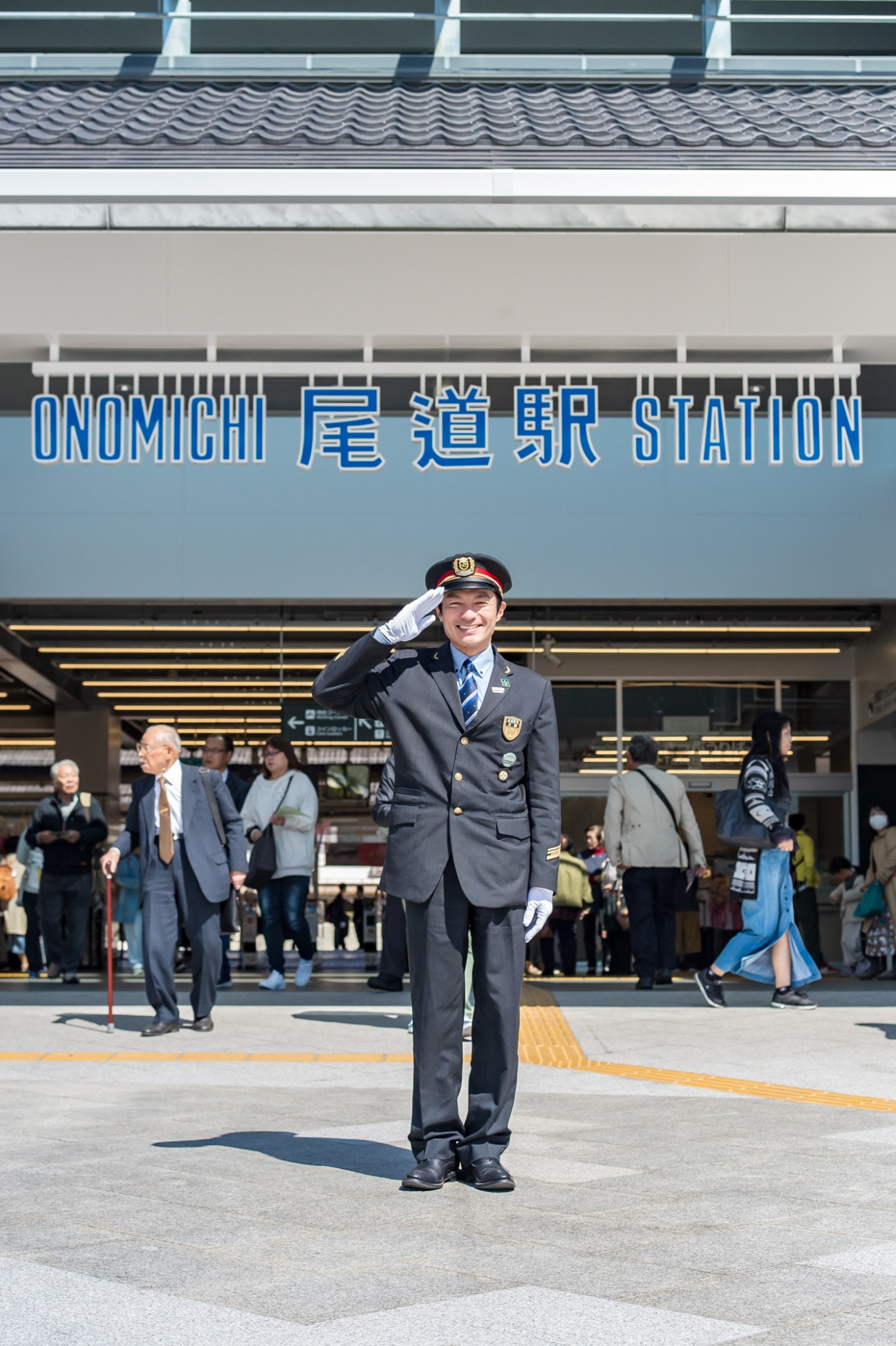 Station chief Shigeki Kataoka salutes in front of Onomichi Station's blue signage.