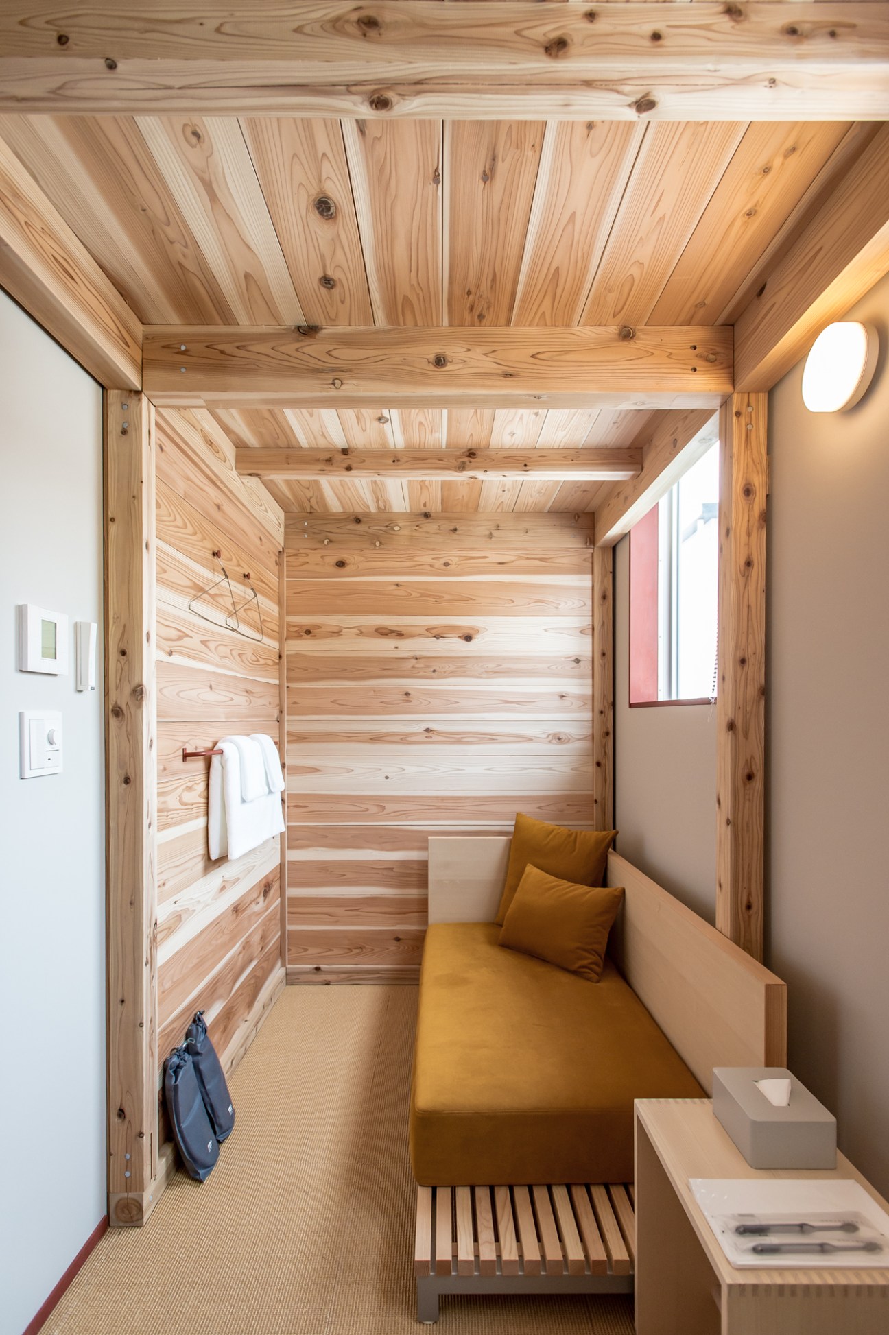 Minimal hostel room with wooden walls, ceiling, mustard-yellow bedding, and simple furnishings.