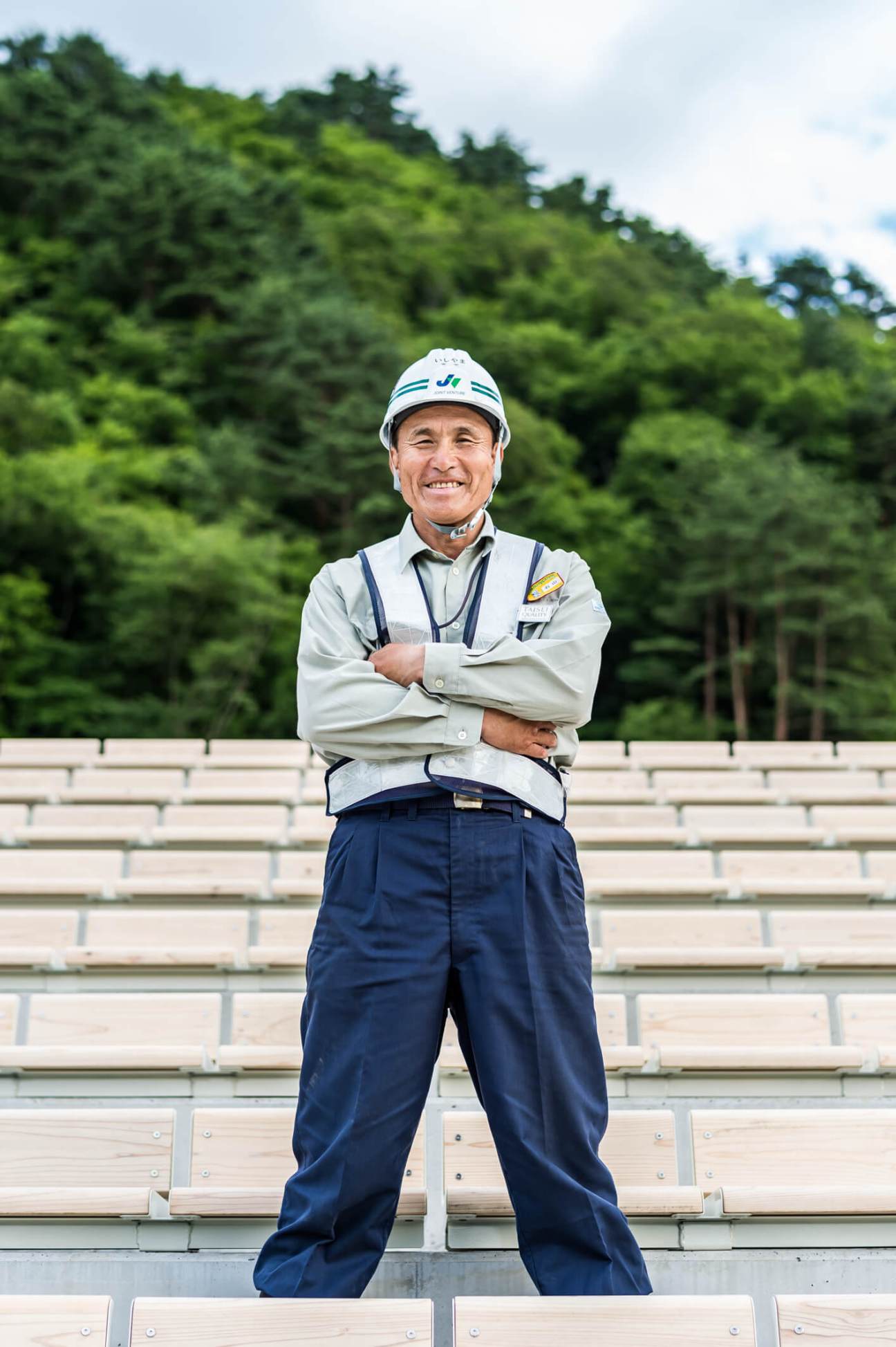 Former Japan rugby player Jiro Ishiyama stands smiling in construction attire at Kamaishi Unosumai Memorial Stadium.