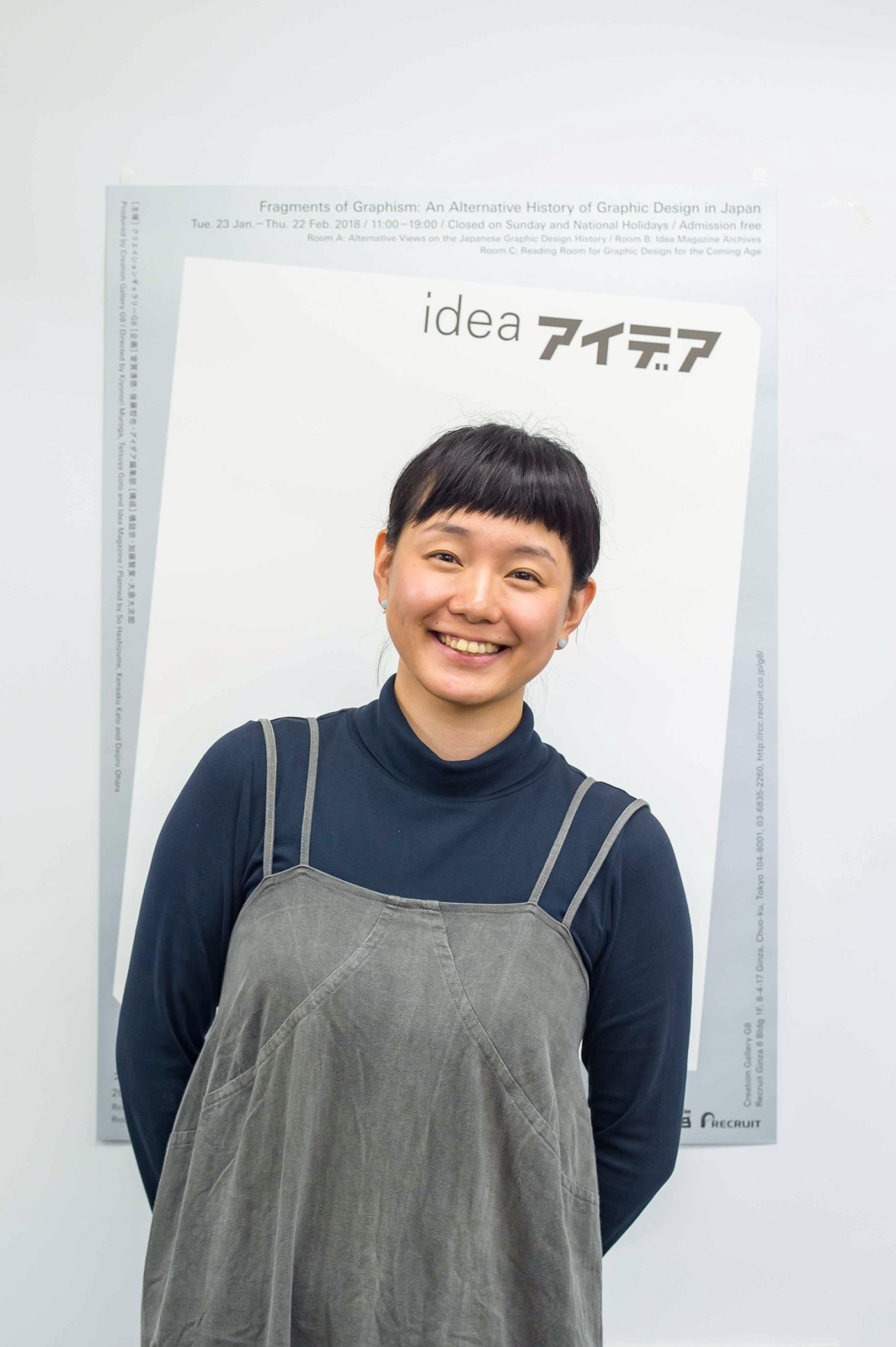 Portrait of Madoka Nishi, editor in chief of Idea magazine, smiling in front of exhibition poster