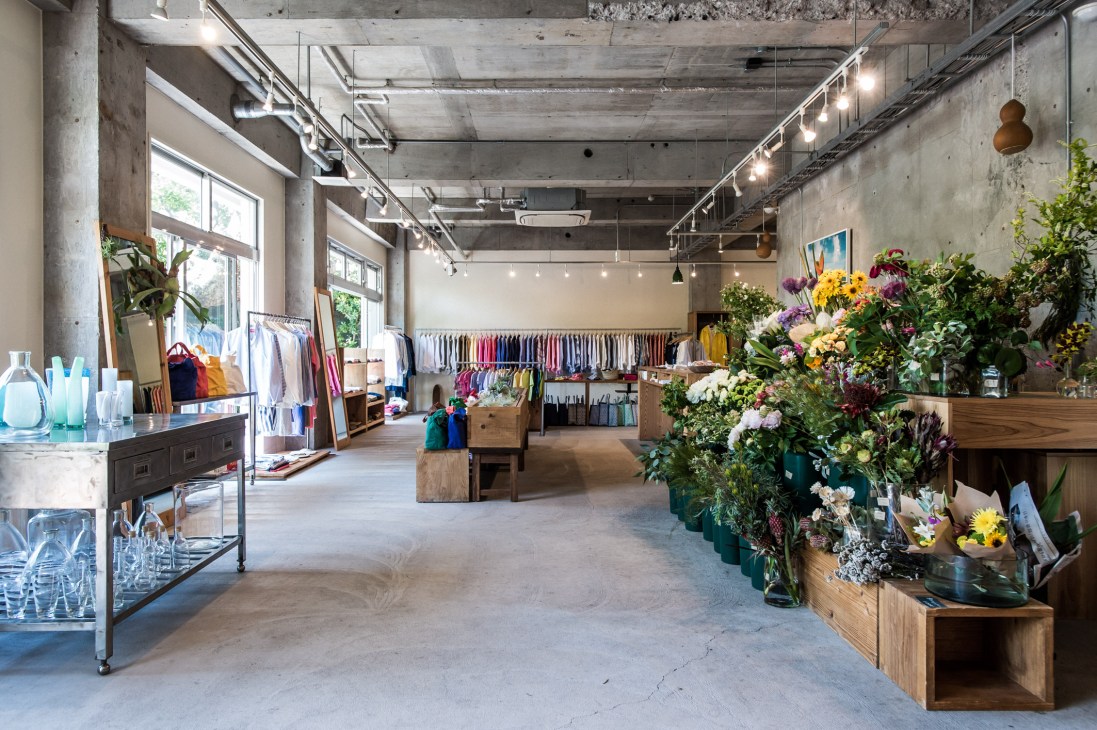 Interior of Sunshine + Cloud shop in Hayama with concrete walls, colorful flowers, clothing racks, and wooden furnishings.