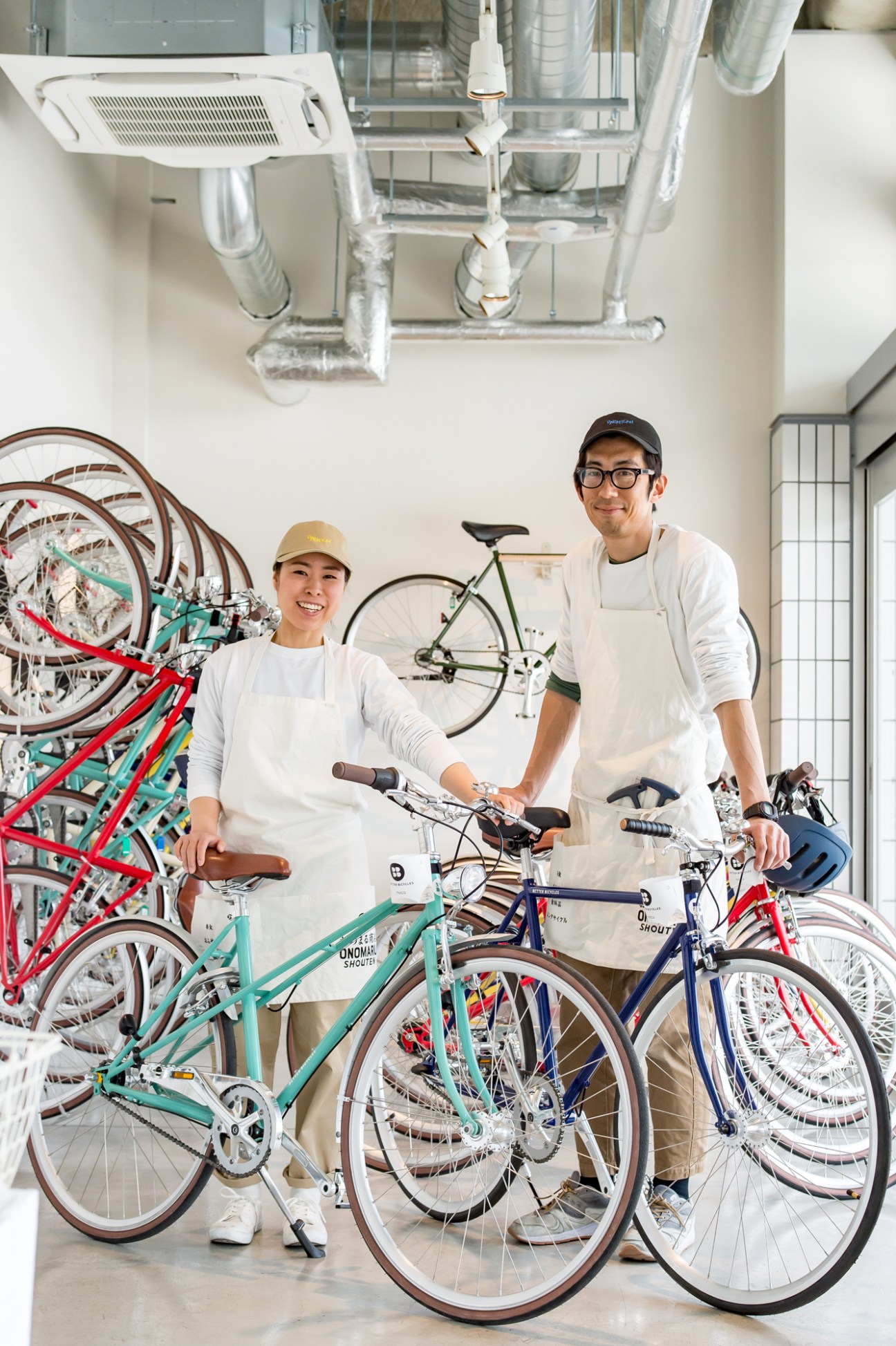 Two staff members stand with rental bicycles in a bright white room at Onomichi Station.