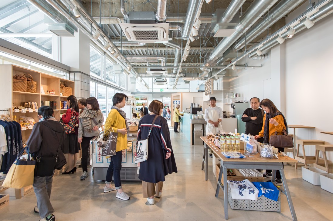 Interior of Onomaru Shouten shop with customers browsing local products and souvenirs under industrial ceiling.
