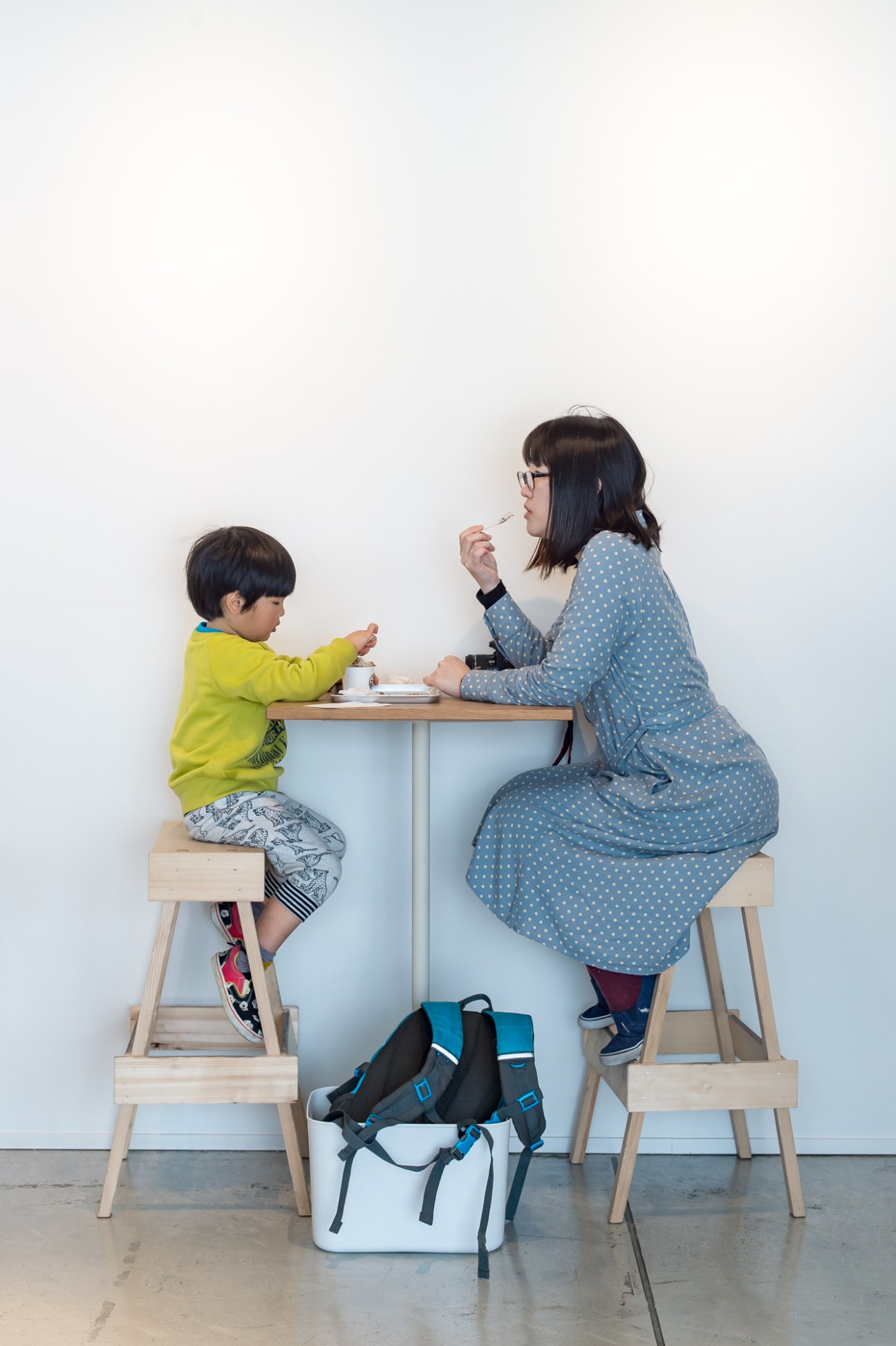 Woman and child sitting at a small wooden table eating food together.