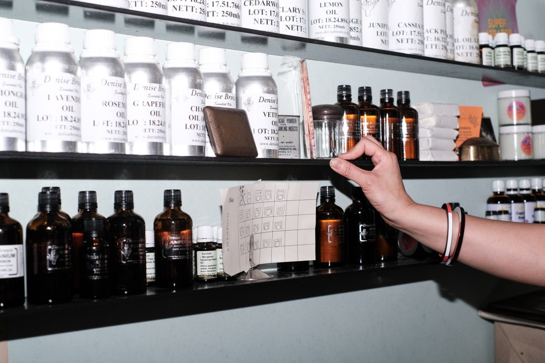 Hand reaching toward shelves displaying bottles of Denise Breton aromatherapy oils with product labels visible.
