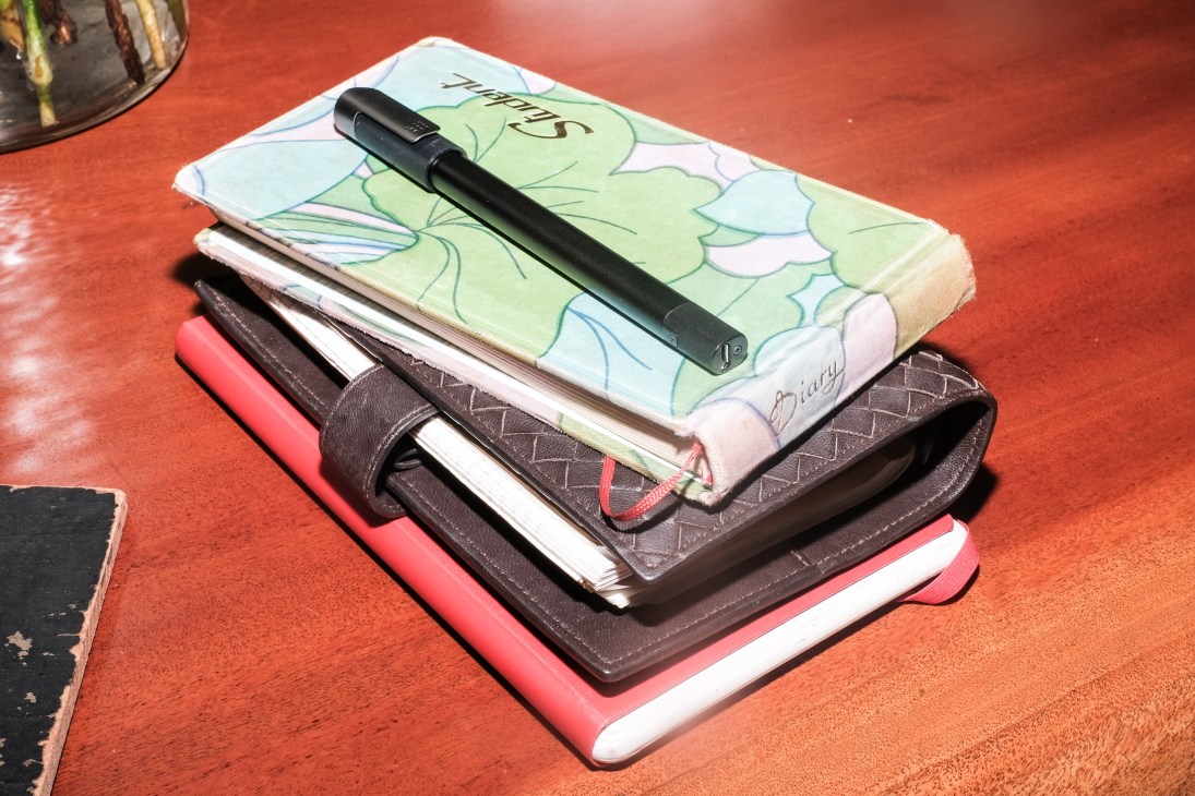 Stack of colorful notebooks and journals with a black pen resting on top