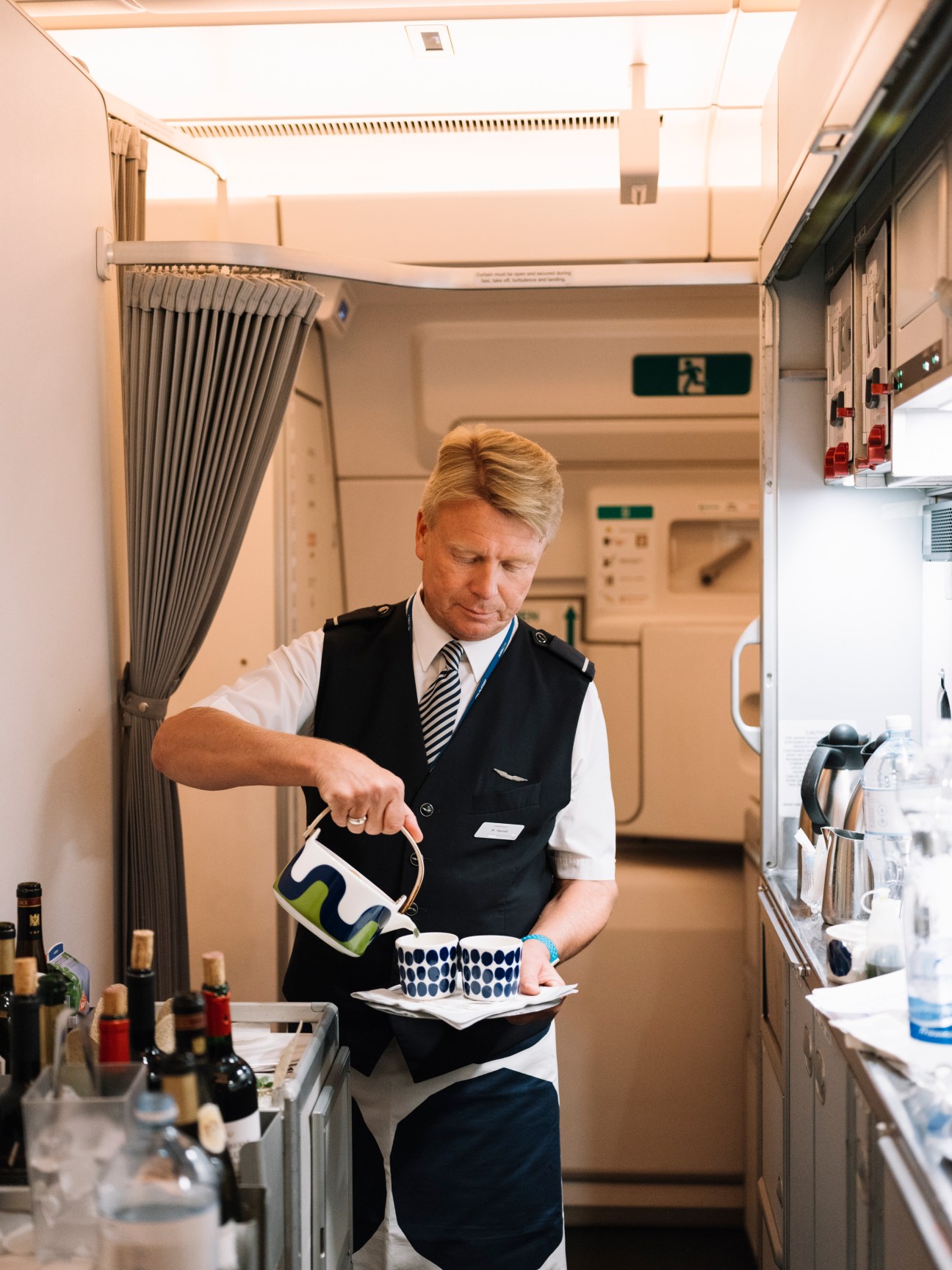 Flight attendant pouring beverage in aircraft galley with Marimekko-patterned cups