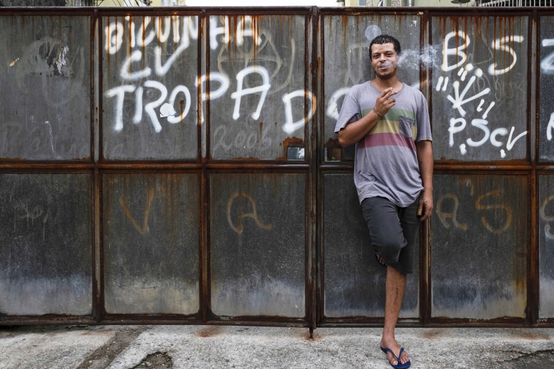 Flavio "Plim Plim", a motorcycle mechanic, stands against a graffitied metal door in Rio de Janeiro.