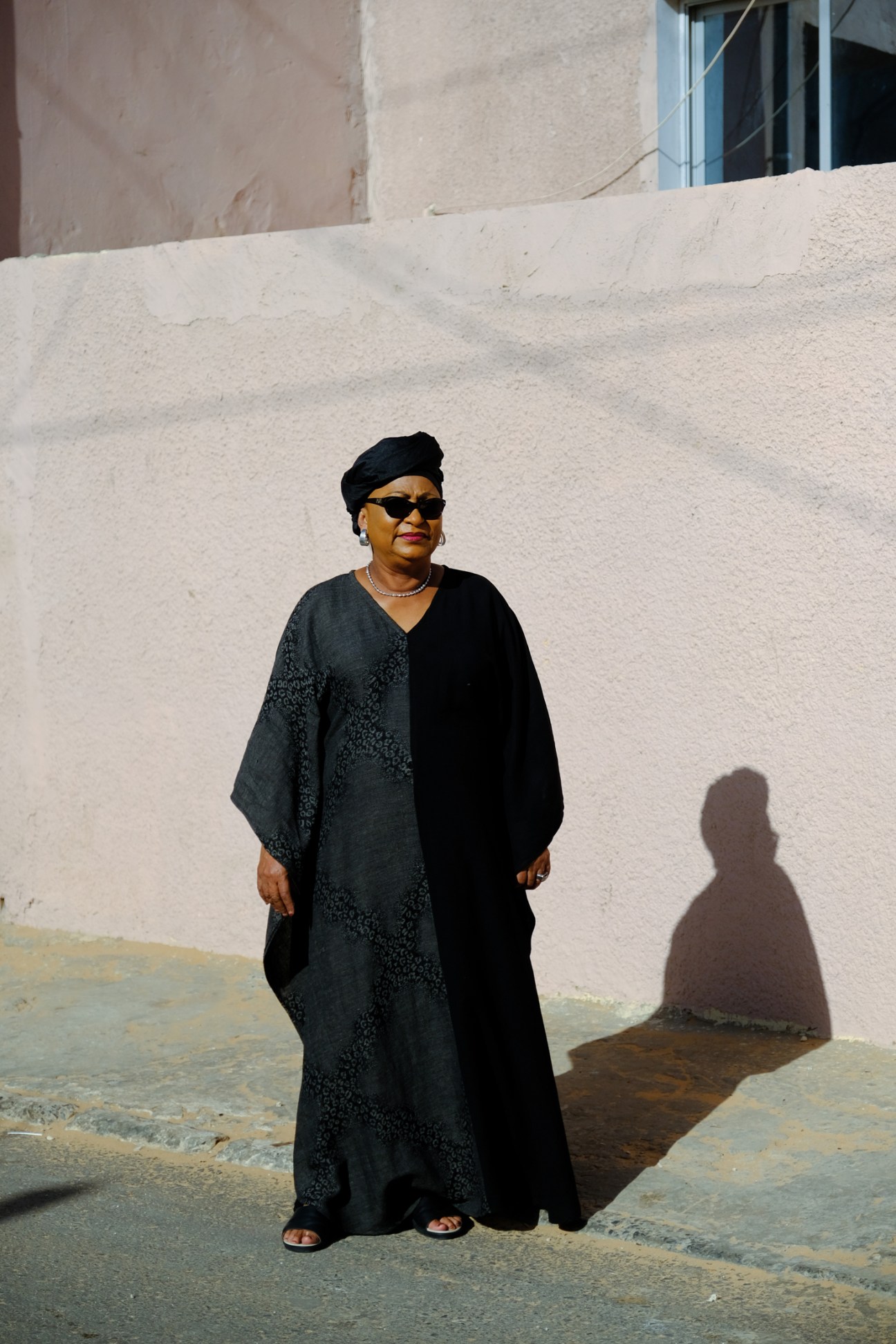 Soham El Wardini, Dakar's first female mayor, wearing black traditional dress and sunglasses against white wall