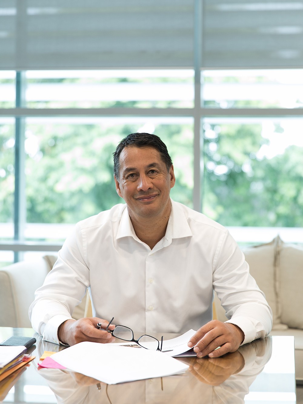 Keith Ikin, CEO of Maori Television, seated at a desk in a bright office with large windows overlooking greenery.
