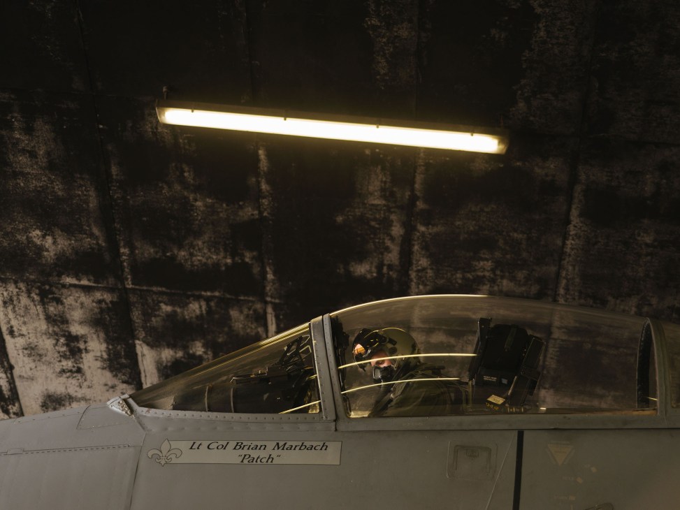 Fighter jet pilot in cockpit under hangar lights, aircraft named 'Lt Col Brian Marbach Patch'