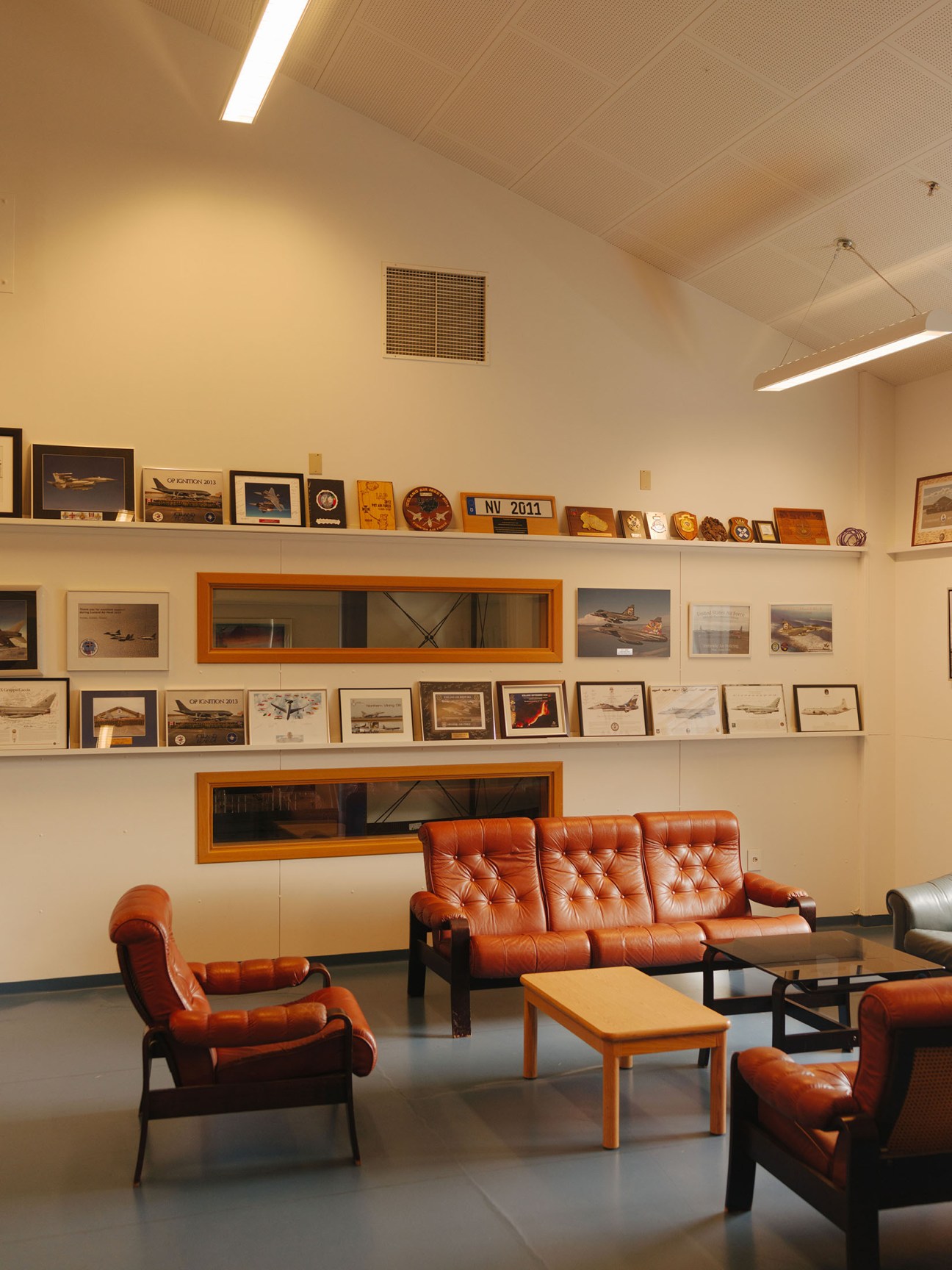 Common area at Keflavík air base with red leather furniture and shelves displaying aircraft memorabilia and squadron insignia.