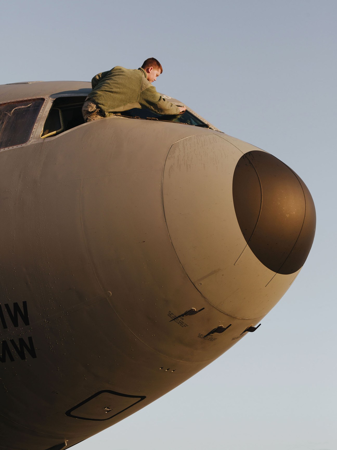 US airman leaning out of KC-10 Extender aircraft window against clear sky