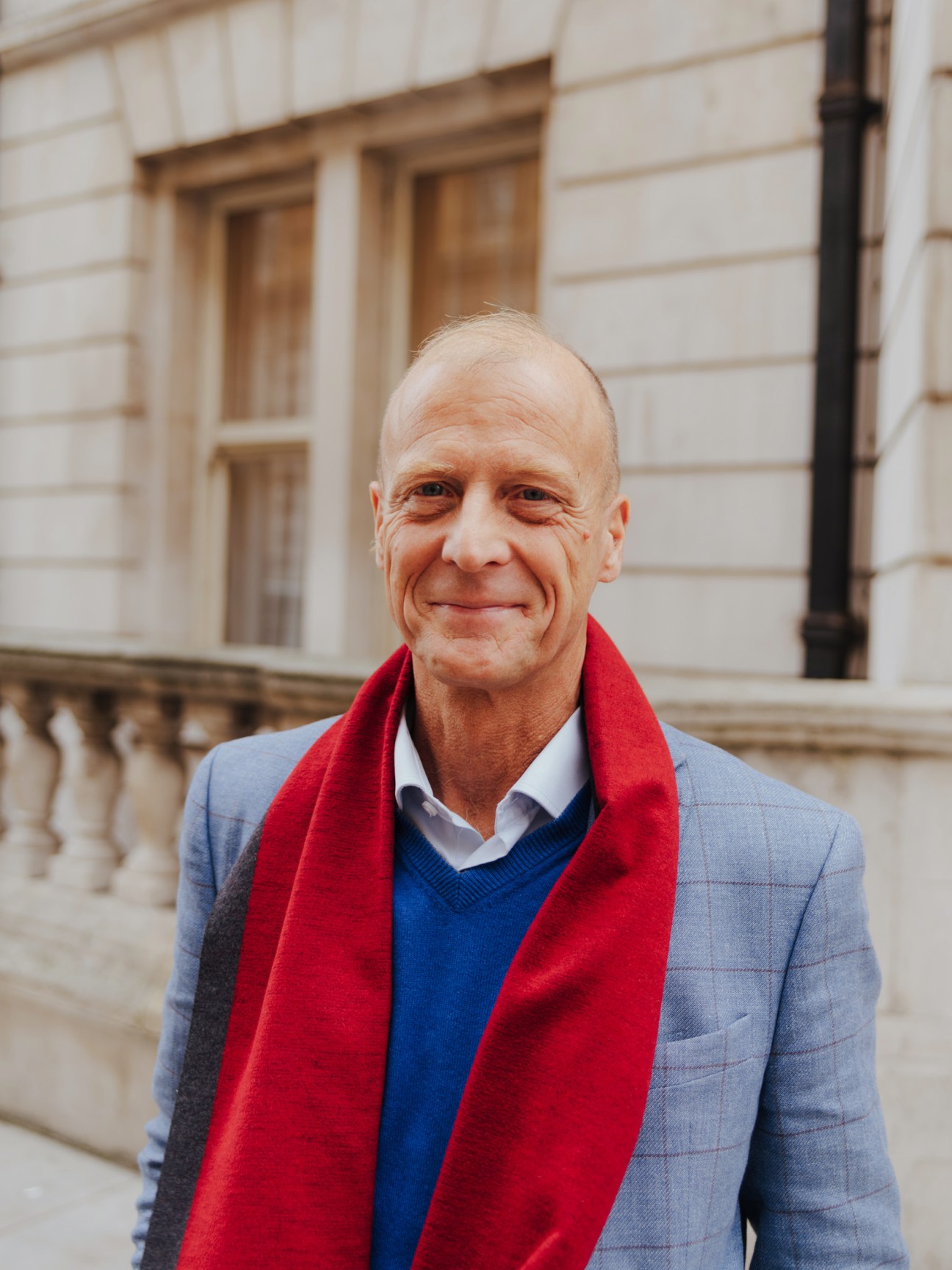 Tom Enders, Airbus CEO, smiling in front of classical architecture while wearing a grey blazer and red scarf.