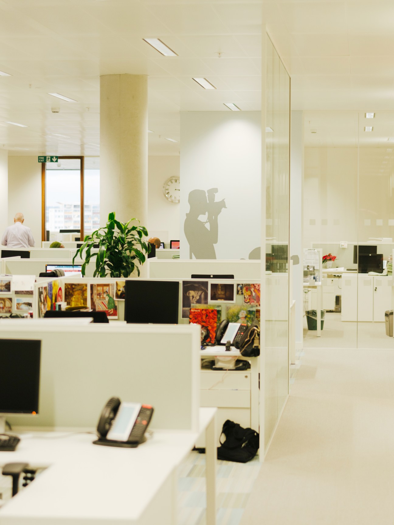Modern office interior with white desks, glass partitions, and silhouette artwork on wall.