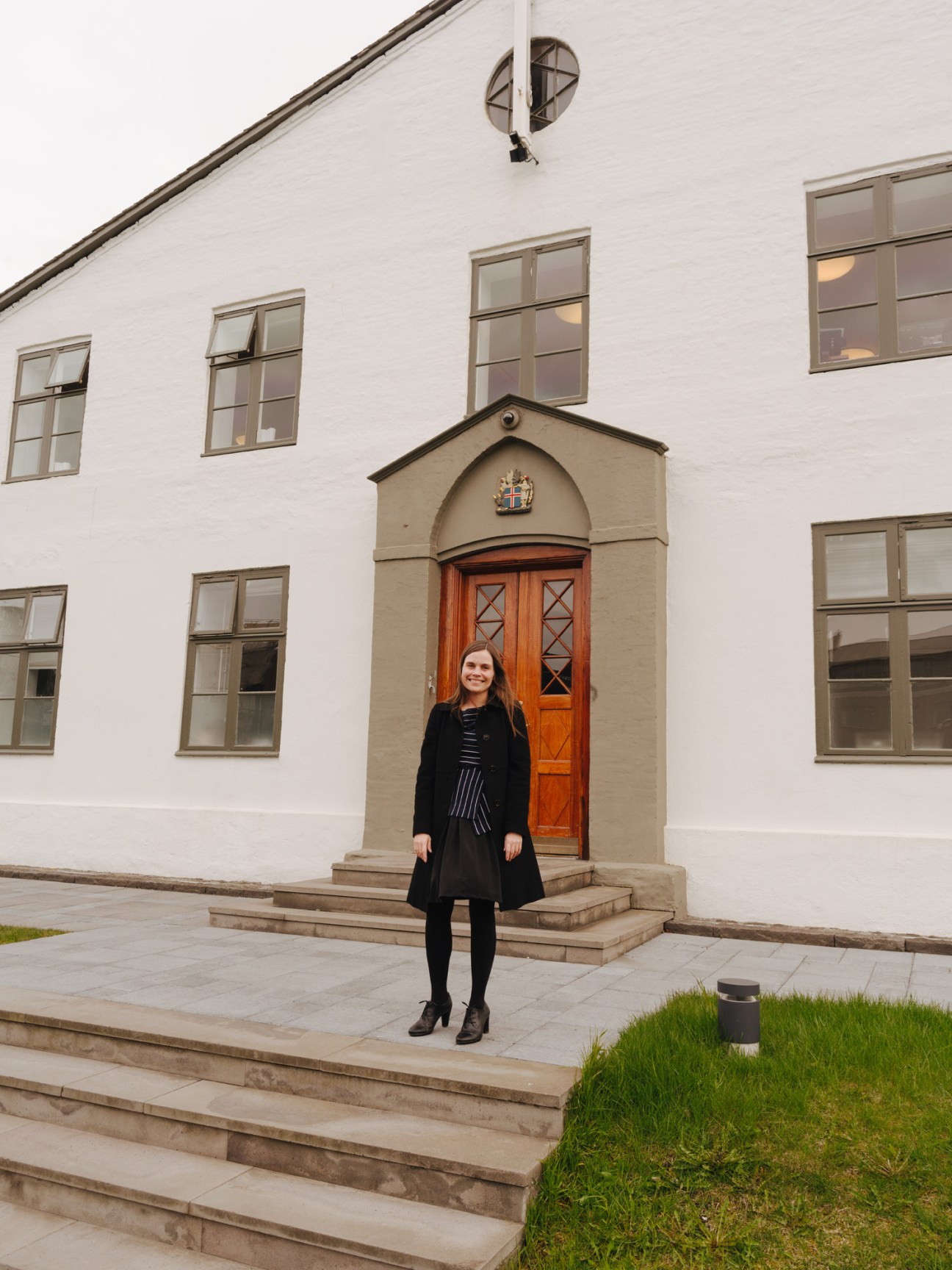Katrin Jakobsdottir stands outside Government House in Reykjavík, a white building with an orange wooden door.