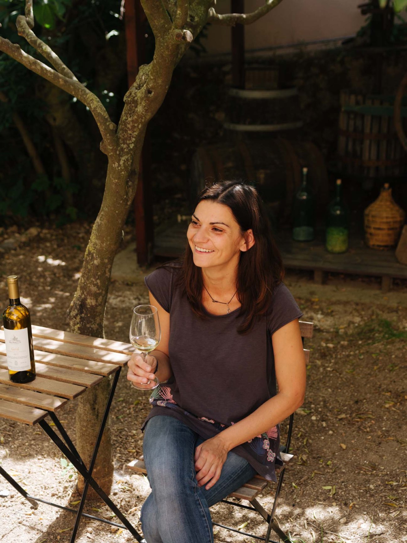 Winemaker Kiki Siamese of Melissinos smiles while holding a glass of white wine outdoors.
