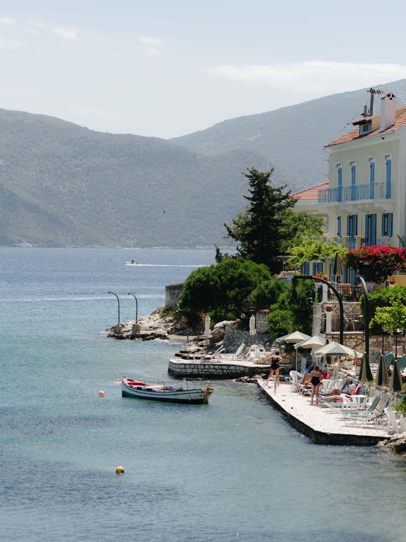 Waterfront village on Kefalonia with white mansion, fishing boats, and forested mountains across the bay.