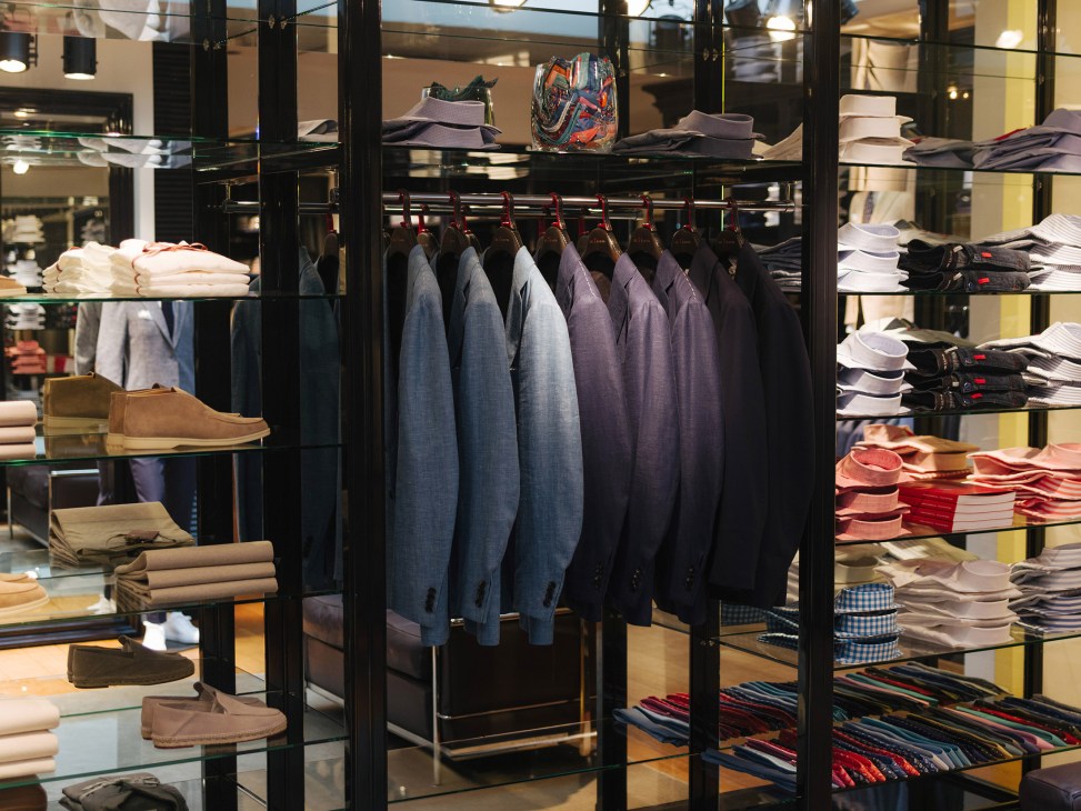 Black metal shelving unit displaying menswear including blazers, shirts, and accessories at Pauw Mannen retail store.