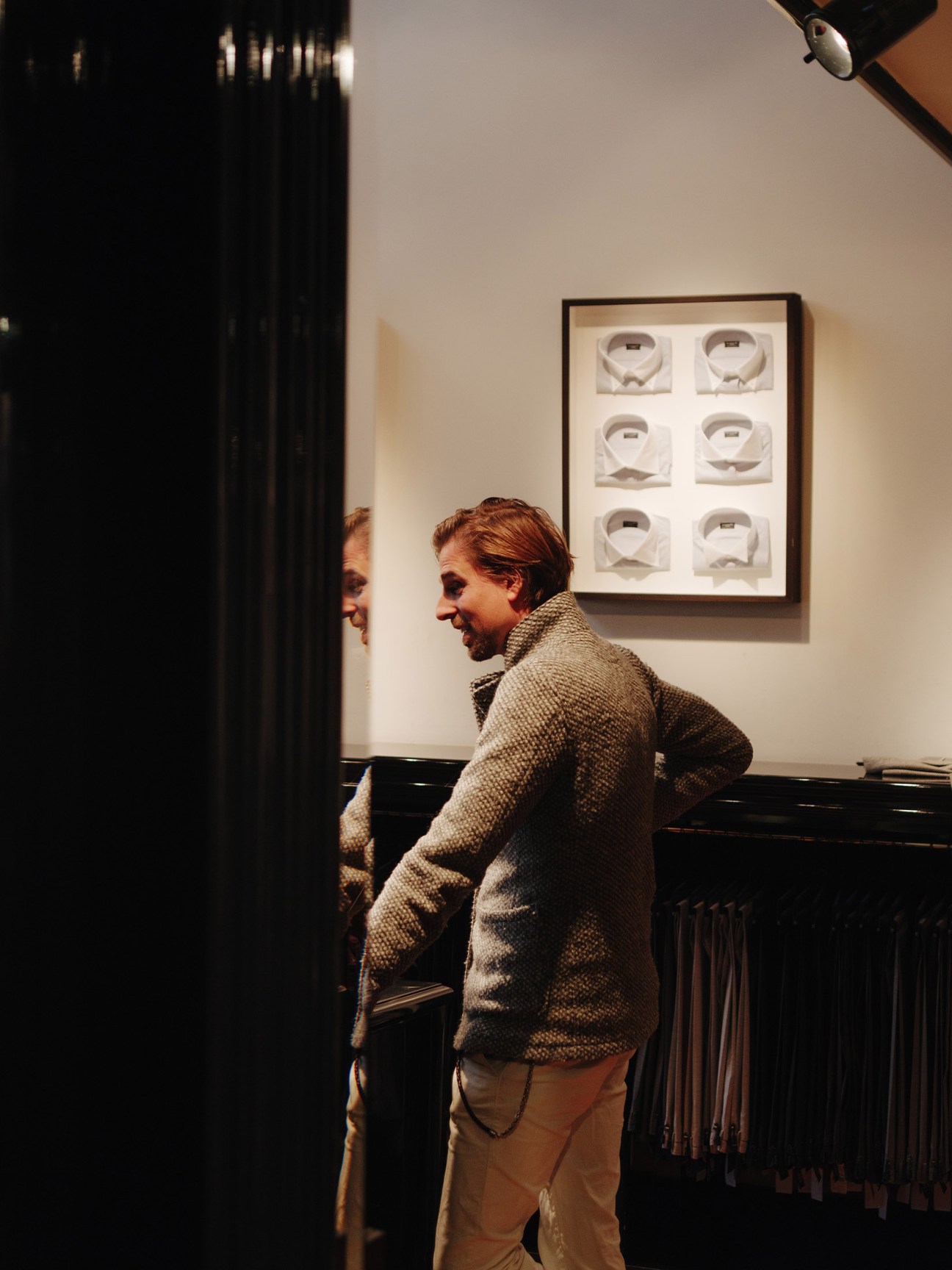 Christiaan Klein-Pauw in a textured cardigan standing in a Pauw menswear shop with tailored pieces displayed behind him.