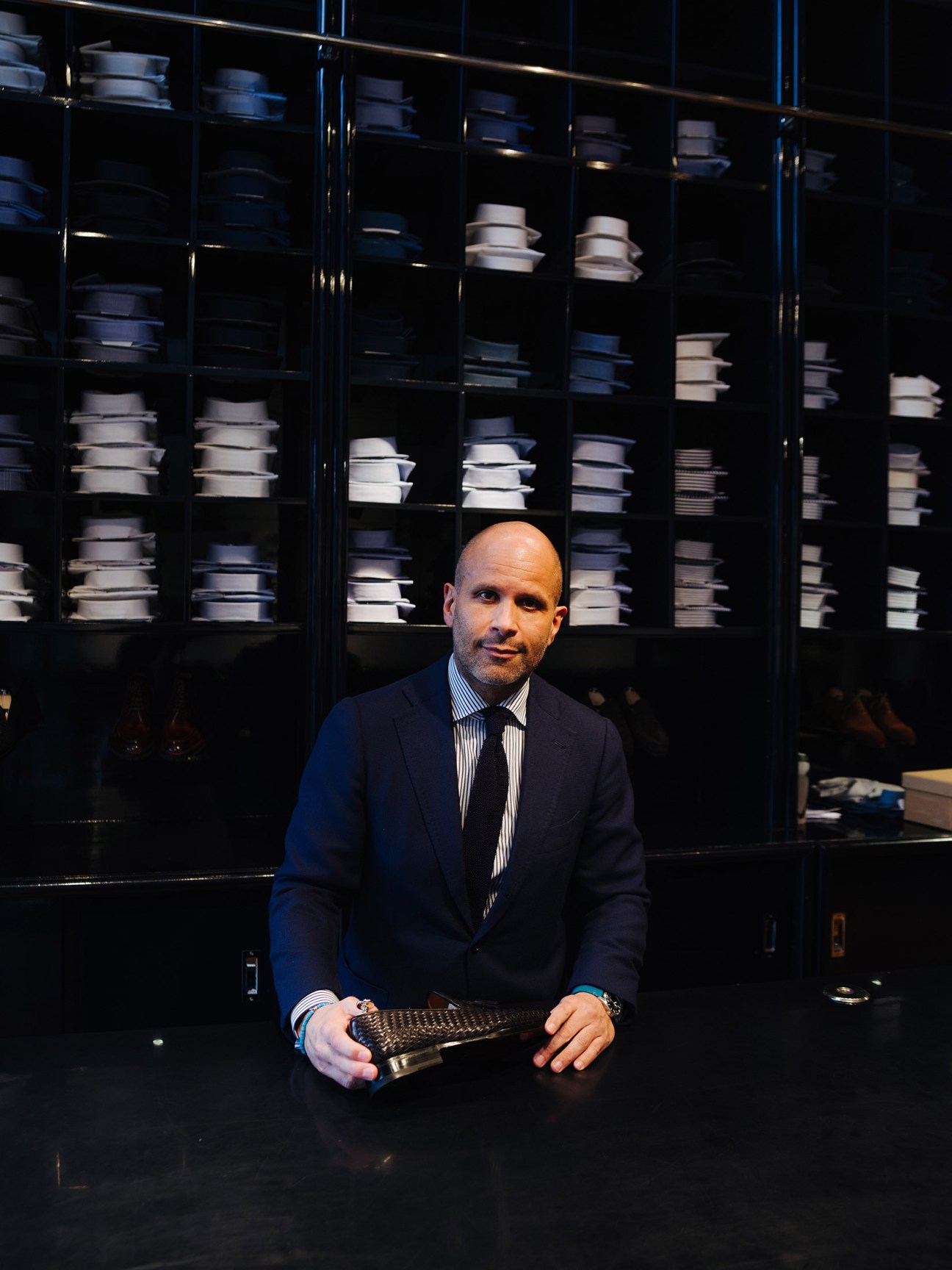 Daniel Meul, store manager at Pauw Mannen, holds a textured black accessory while standing in front of shelving displaying folded garments.