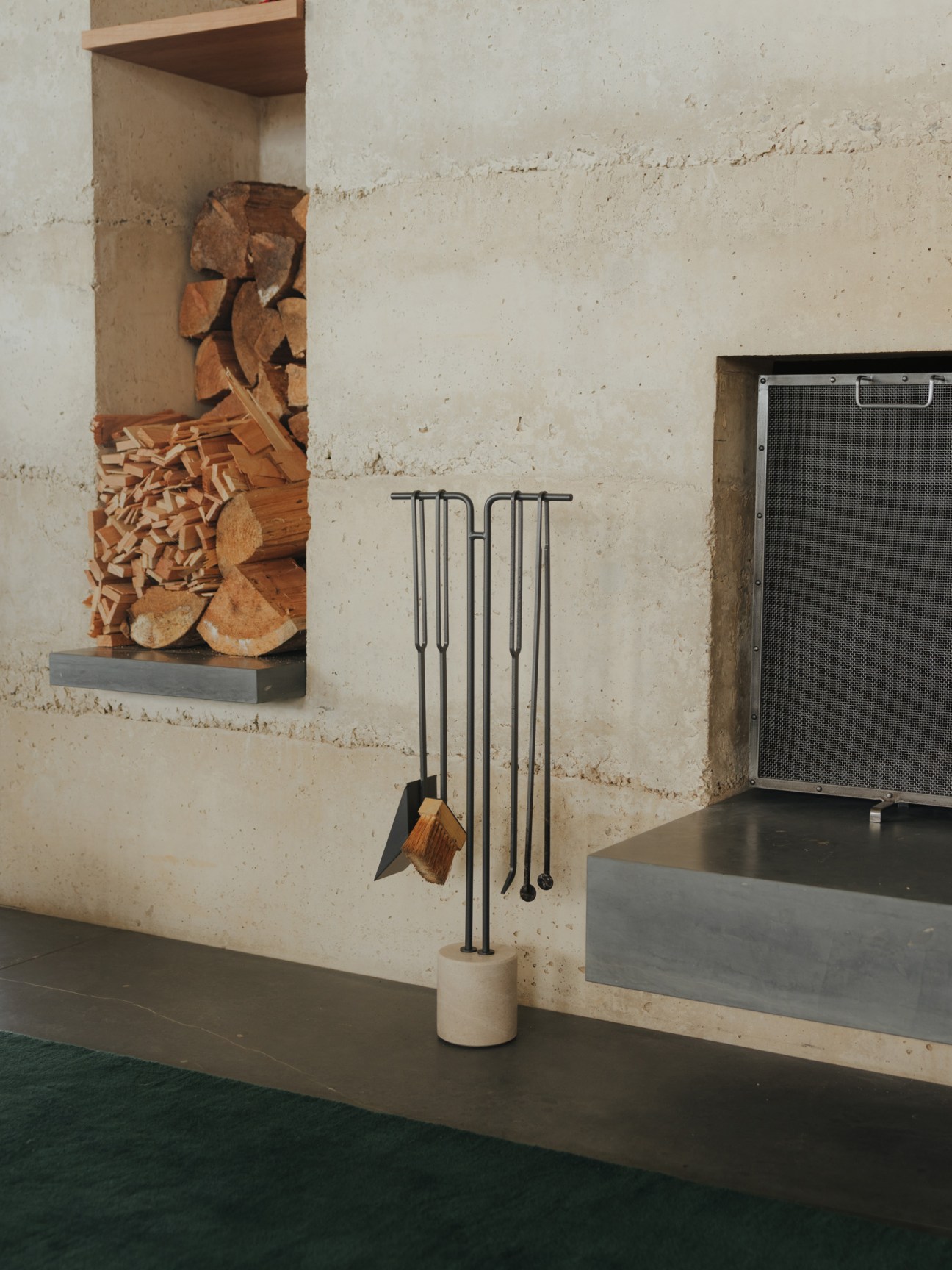 Concrete interior wall with recessed wood storage and fireplace tools in Peter Zumthor's Secular Retreat.