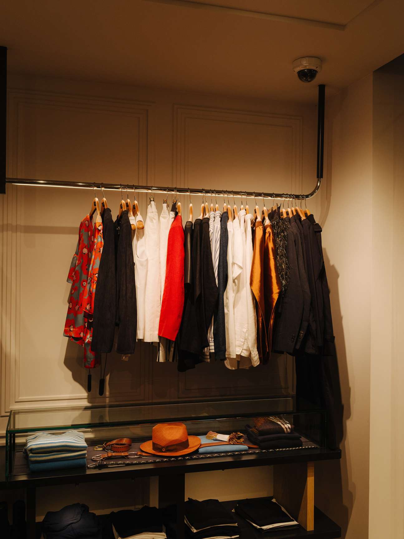 A clothing display featuring new-season womenswear on wooden hangers with an orange hat and accessories on a black shelf below.