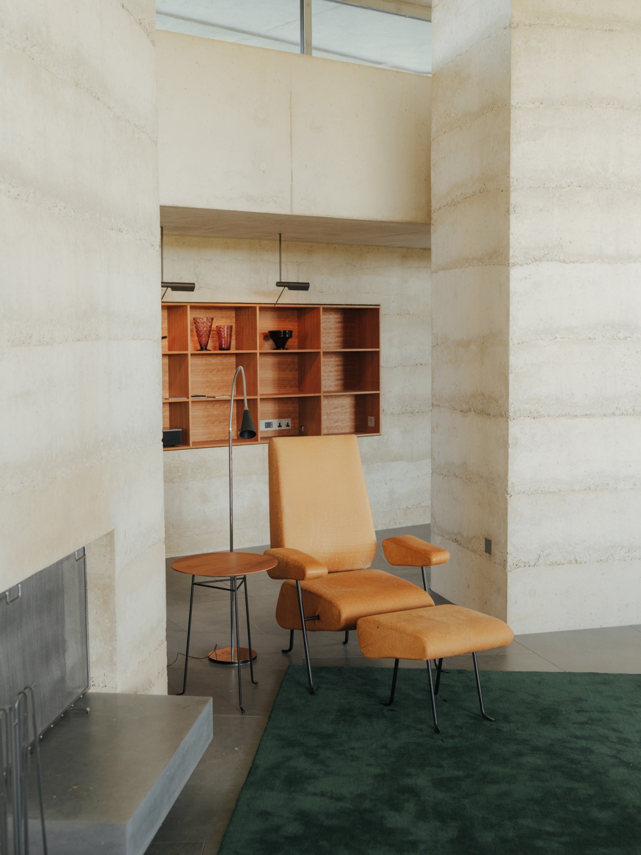 Orange leather armchairs with metal frames and a small side table in a minimalist concrete interior with wooden shelving.