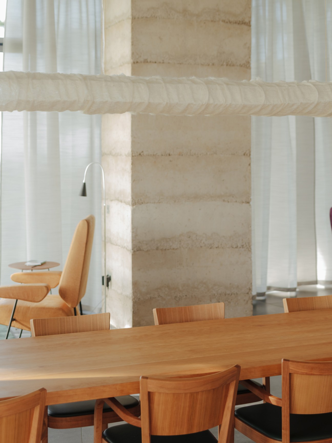 Dining area with wooden table and chairs from the Horgen Glarus collection, concrete columns, and white curtains.