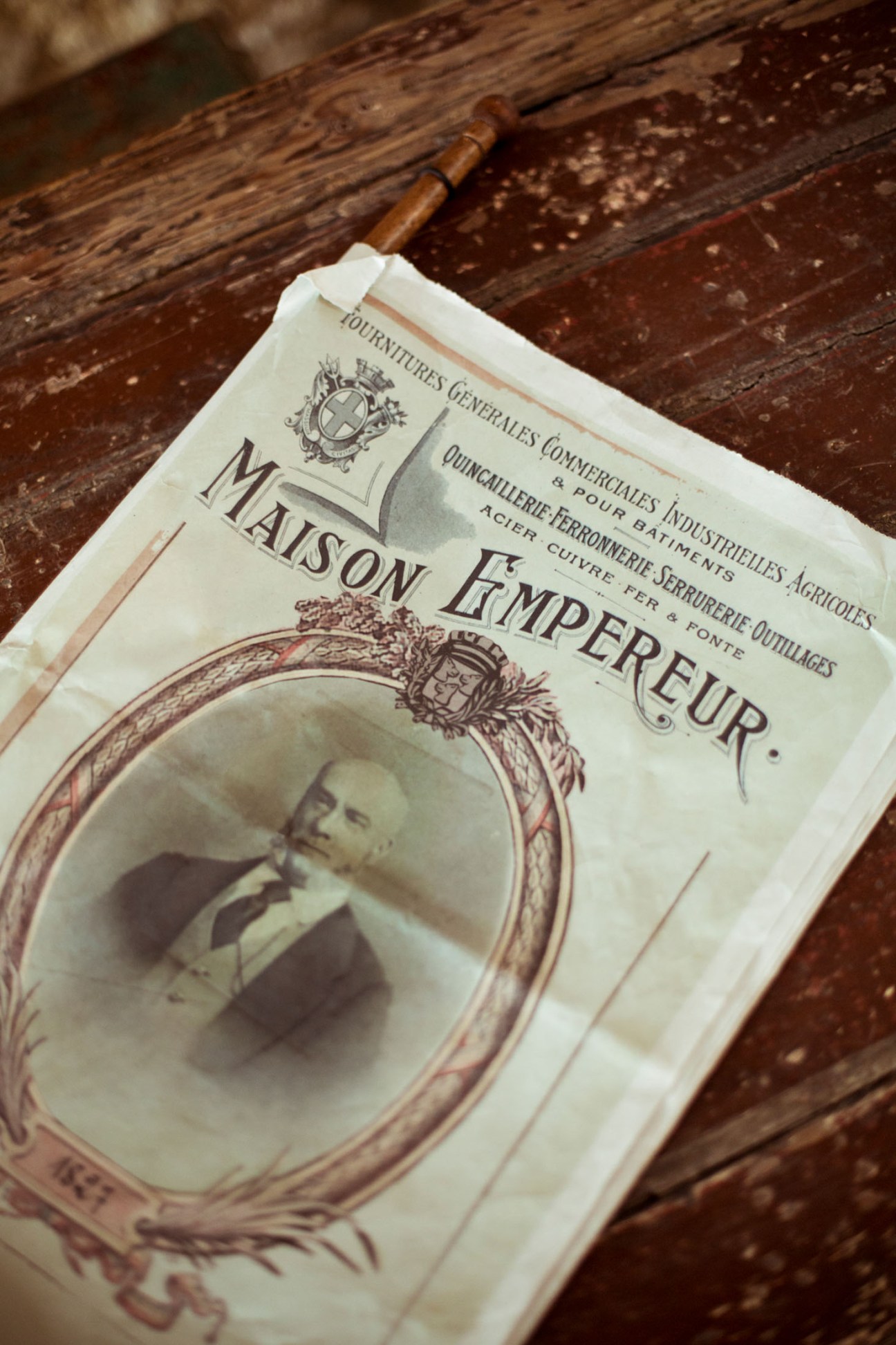 Vintage Maison Empereur newspaper on rustic wooden surface with decorative frame and portrait.