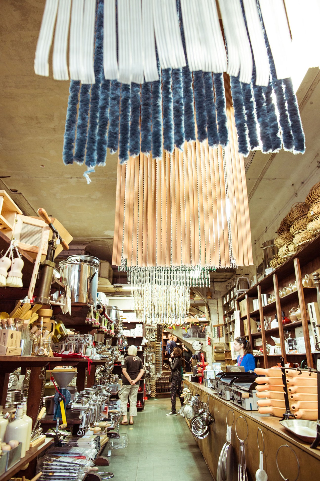 Cloth samples hung from ceiling and wooden shelves stocked with products inside Maison Empereur hardware store.