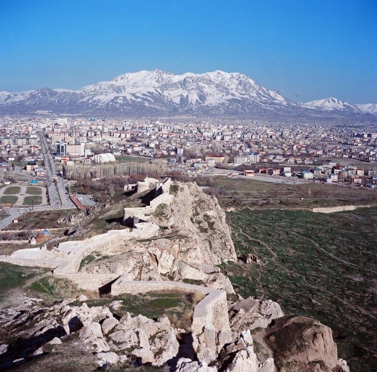 Panoramic view of Van cityscape with snow-capped mountain in background and ancient fortress ruins in foreground.