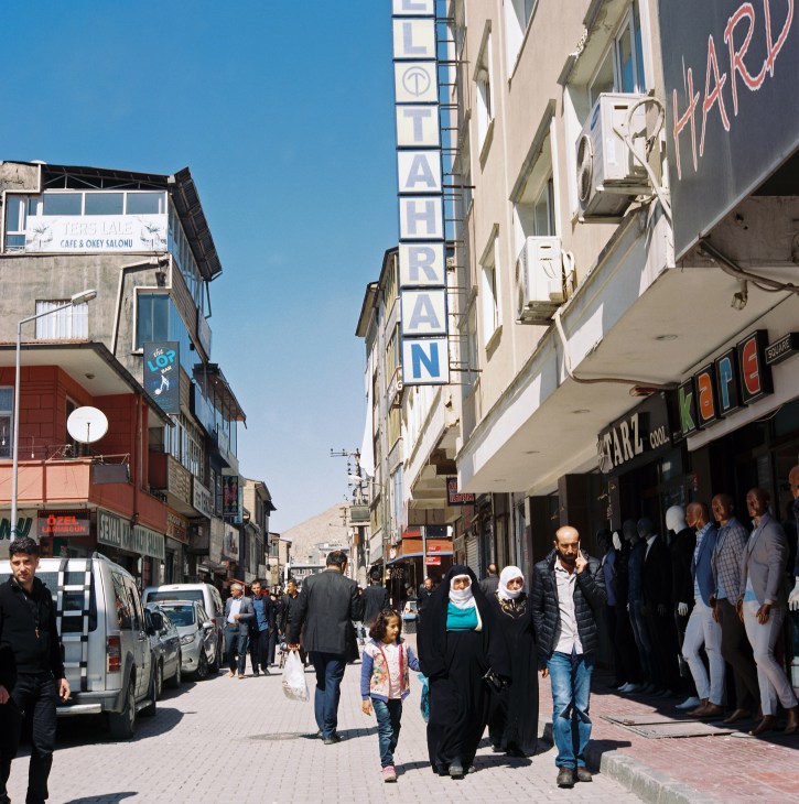 Busy shopping street in Van with pedestrians and storefronts under clear blue sky.