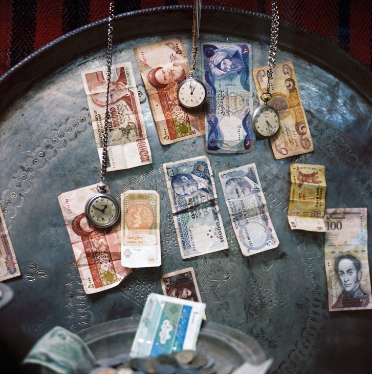 Iranian and British banknotes and pocket watches arranged on a decorative metal plate.