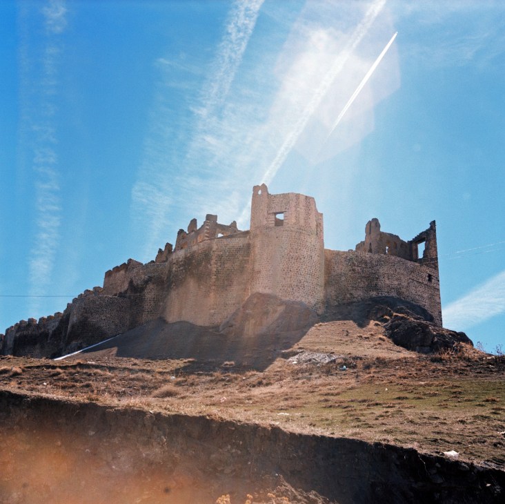 Hosap Castle, a medieval Ottoman fortress with stone towers and crenellations overlooking bare hills under blue sky.