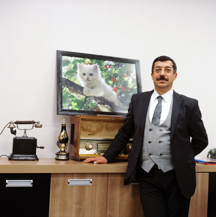 Sinan Bagli, head of culture and tourism in Van, stands in an office next to a framed portrait of a white Van cat with mismatched colored eyes.