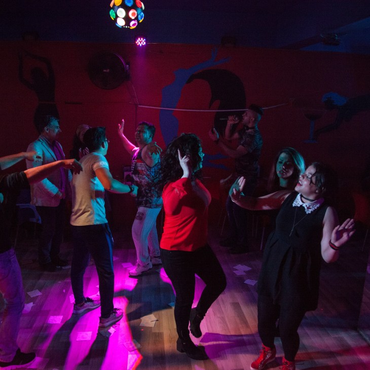 People dancing in a nightclub with colorful neon lighting and disco ball overhead.