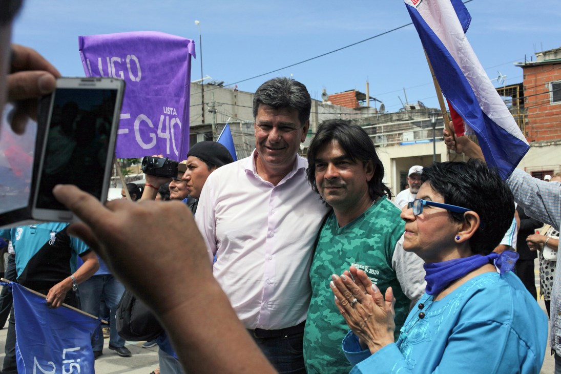Efraín Alegre campaigning surrounded by supporters holding blue and purple flags at a rally.