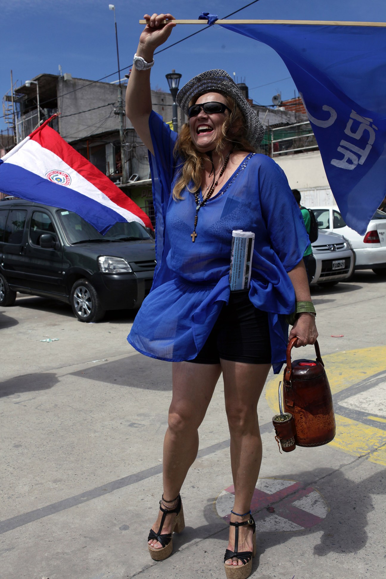 Woman wearing blue holding Paraguayan flag and Alianza Ganar banner at campaign rally.
