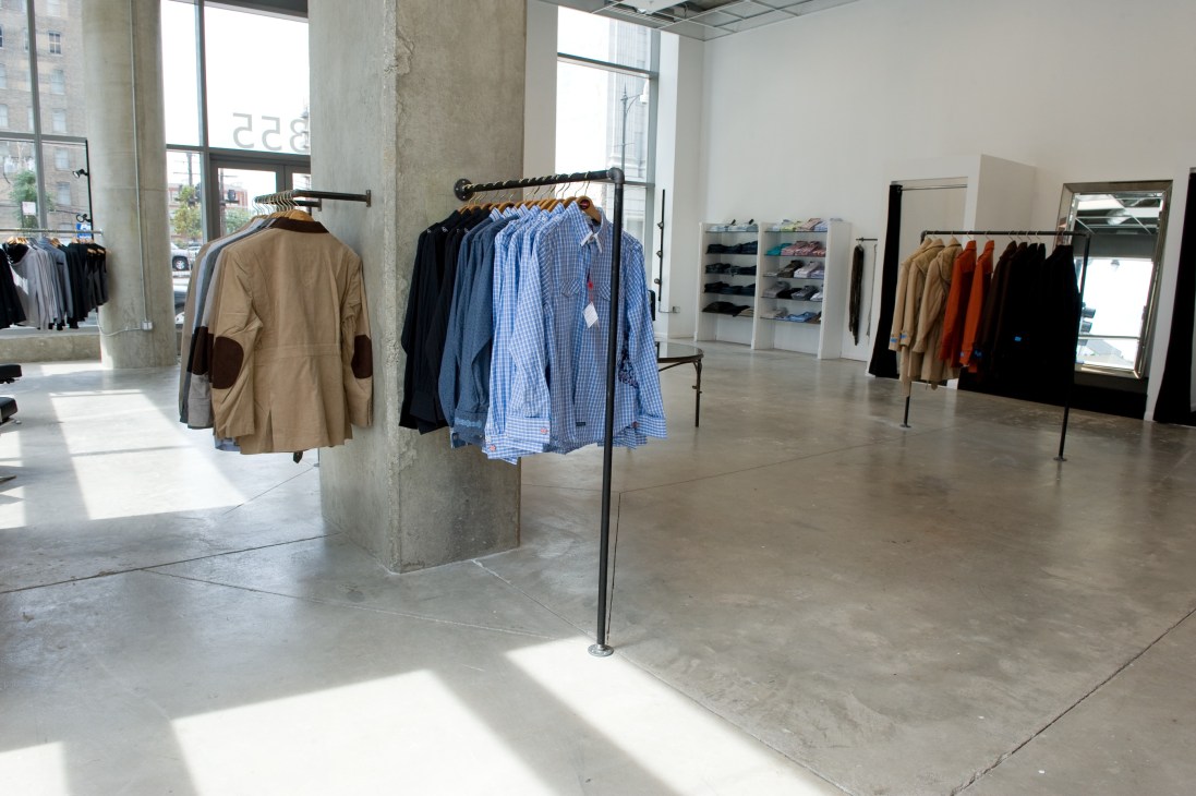 Entourage Man menswear boutique interior with clothing racks and concrete columns.